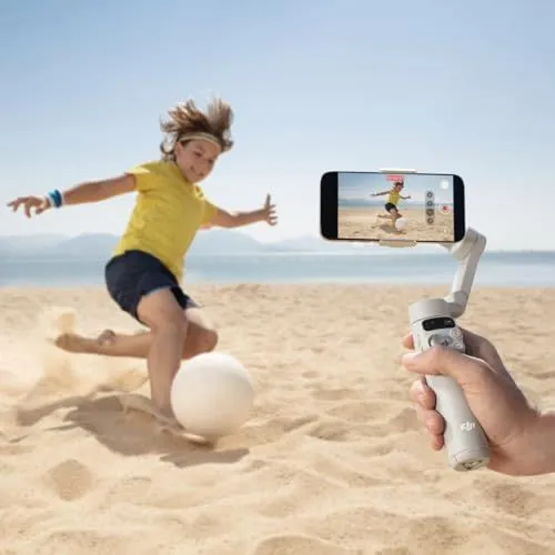 A handheld gimbal capturing a child playing soccer on a beach