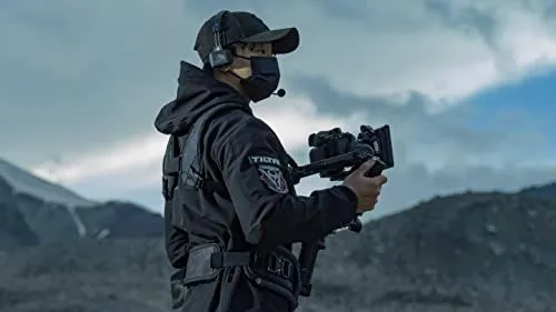 A professional camera operator filming in a rugged mountainous landscape