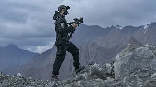 A professional filmmaker standing on a rocky mountain ridge