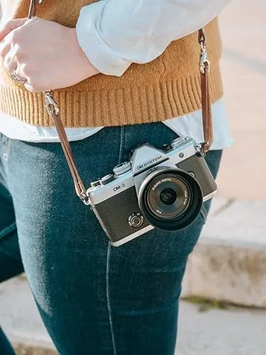 A Silver OM System OM-5 Mirrorless Camera with a Leather Strap