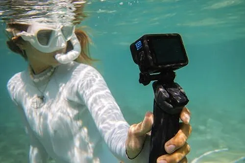 A woman snorkeling while holding an action camera underwater
